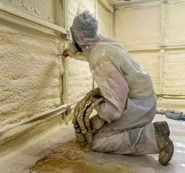 insulation installer, suited in PPE gear, insulating closed cell insulation, in walls of a home.