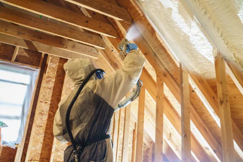 Open cell spray foam installer insulating home's ceiling.