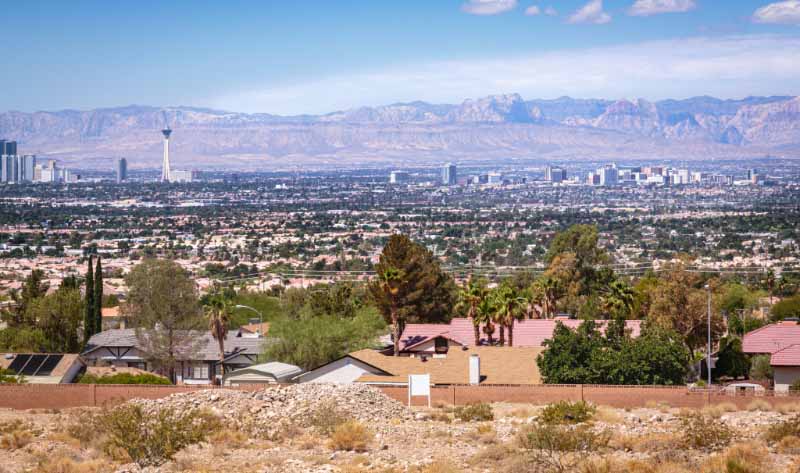 Elevated view across a Las Vegas suburban neighborhood toward the Strip skyline, with the Stratosphere Tower and Spring Mountains rising beyond the desert landscape on a clear day.