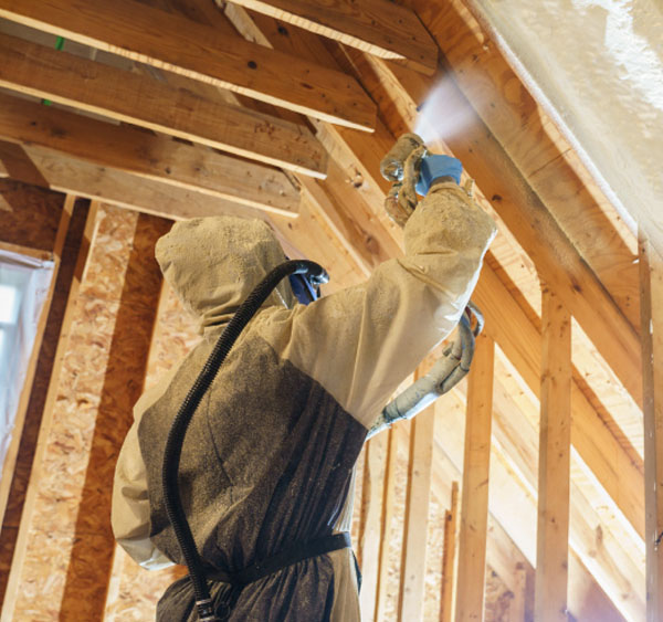 Battle Born Specialties worker in protective gear standing beside fiberglass batt insulation in a framed wall cavity.