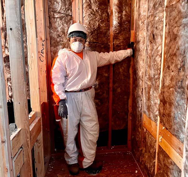 Battle Born Specialties technician in protective suit spraying foam insulation between attic roof rafters.