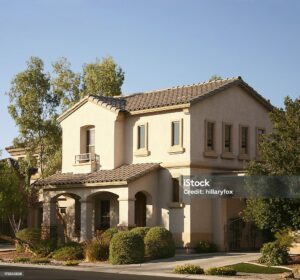 Two-story Mediterranean-style house with arched porch, tile roof, and surrounding greenery